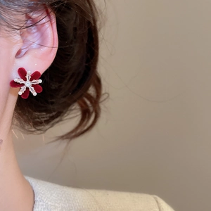 Detailed close-up of a burgundy flocked flower earring with zircon and pearls on a model