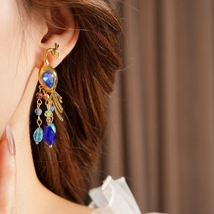 Close-up of vintage gold peacock earring with blue gemstone and colorful beads on ear