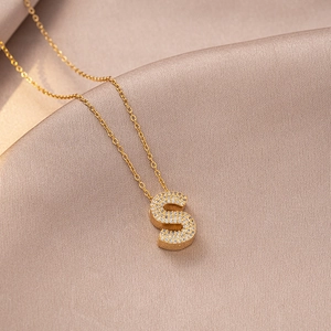 Macro shot of gold S-letter pendant necklace with zircons on champagne silk fabric
