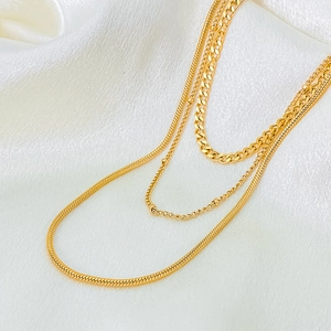 Detail of layered gold chains including snake and curb styles on white silk fabric