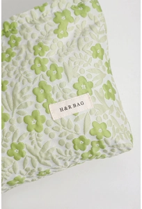Detailed close-up of emerald floral jacquard fabric and brand tag on makeup bag