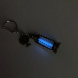 Glow-in-the-dark blue liquid hourglass keychain with metallic tree-shaped pendant charm