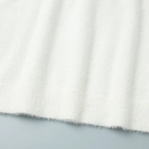 Close-up of white plush knit fabric texture with ribbed cuff detail on sleeve