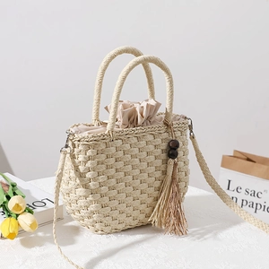 Beige straw tote bag with tassel decor and drawstring lining on a rustic white table