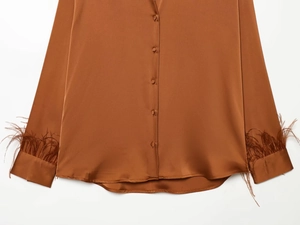 Detail of brown satin blouse featuring feather-trimmed cuffs and elegant button closure