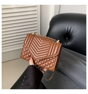 Detail of brown quilted chain bag featuring V-shaped stitching and gold-tone metal strap