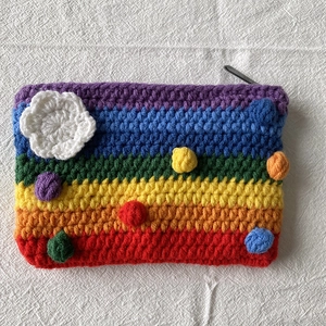 Detail of colorful knitted rainbow coin purse with crochet flowers and fluffy pom-poms