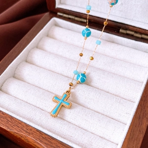 Detail eines goldenen Kreuzanhängers mit blauer Emaille und Perlen auf Samttablett