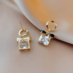 Détail de boucles d'oreilles nœud doré avec zircon carré sur tissu en soie champagne