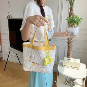 Detailed close-up of a white quilted floral tote bag with embroidery and sunflower charm