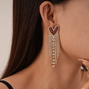 Macro shot of gold heart earrings with red gemstones and long tassels on a model