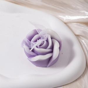 Detail of rose-shaped scented candle with purple gradient and white decorative ribbon