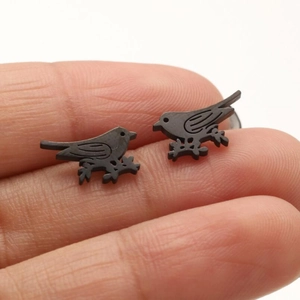 Close-up of matte black bird on branch stud earrings held on a finger for size