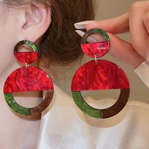Detail of large acrylic geometric earrings in marbled red and dark green finish on model