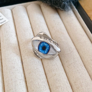 Makro-Ansicht des silbernen Evil-Eye-Rings mit blauer Pupille auf beigem Samttablett