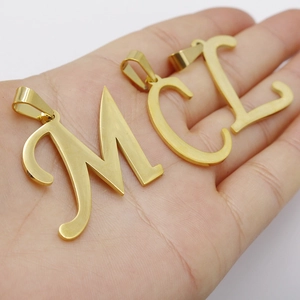 Handheld gold stainless steel alphabet pendants featuring letters M, C, and L on palm