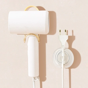 Soporte de pared dorado para secador de pelo con organizador de cables en fondo rosado