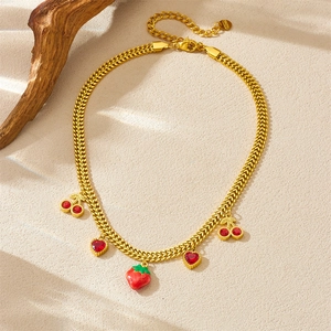 Gold stainless steel chain necklace with cherry, strawberry and heart pendants on sand