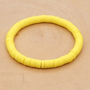 Detailopname van een felgele Heishi-armband van polymeerklei op een houten ondergrond