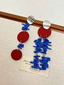 Detailed close-up of blue shell tassel earrings with red accents on artistic wooden background
