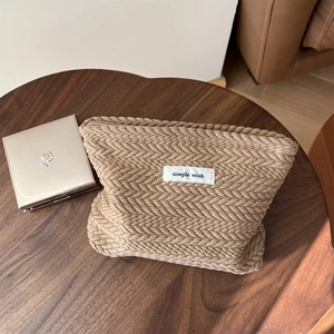 Macro detail of beige woven makeup bag with V-shaped herringbone texture and metal zipper