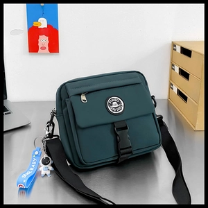 Detail view of dark green nylon messenger bag with astronaut charm and buckle on metal desk