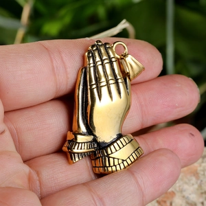 Close-up of a golden praying hands pendant with detailed texture held in hand