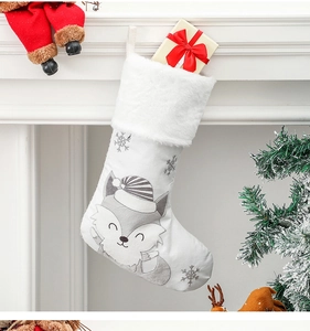 Dettaglio calza di Natale in peluche bianca con motivo a volpe e scatola regalo vicino