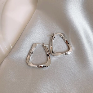 Macro detail of silver geometric hoop earrings on elegant silk fabric background