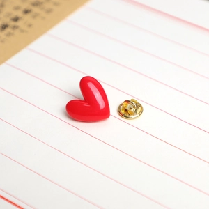 Red heart enamel pin with gold butterfly clutch on a white lined notebook page