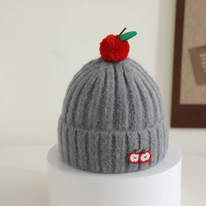 Detail of grey knitted hat featuring a red apple pom-pom and cute fruit embroidery