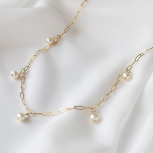 Close-up of golden Cuban chain necklace with small round pearls on white silk