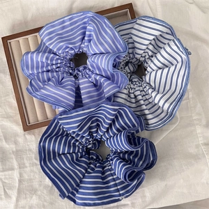 Set of three blue and white striped fabric scrunchies on a wooden tray for hair styling