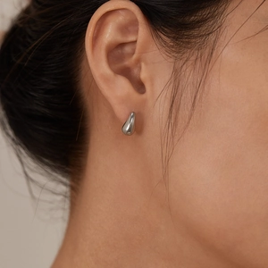 Polished silver teardrop earrings shown in a side close-up on a model's ear