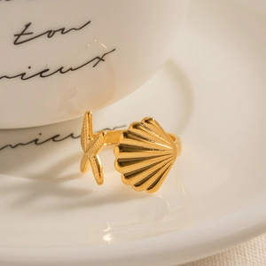Detailed view of a gold starfish and seashell open ring on a white ceramic plate