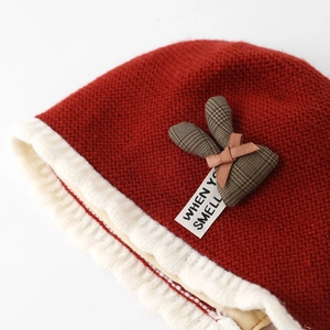 Close-up of deep red baby knit hat with plush white trim and plaid bunny ears detail
