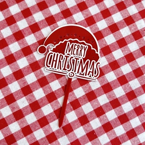 Detail of red and white acrylic Merry Christmas cake topper on a checkered tablecloth