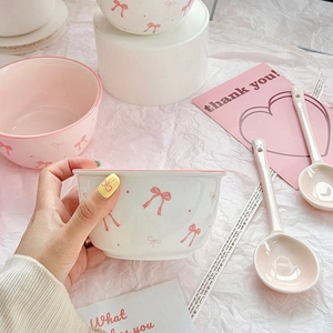 Detail of hand holding a cute white ceramic bowl featuring a pink bow tie pattern and spoon