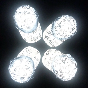 Top view of four reflective silver baseball caps with shiny letter prints on black background