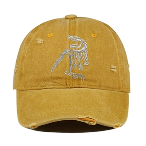 Close-up of mustard yellow distressed baseball cap with dinosaur skeleton embroidery.