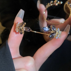 Close-up of gold leaf bracelet with navy and white marquise-cut gems on dark background