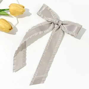 Detailed view of silver satin bow hair clip with ruffle edges and long streamers