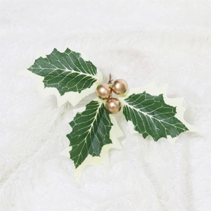 Close-up of artificial green holly leaves with white edges and gold berries for DIY decor