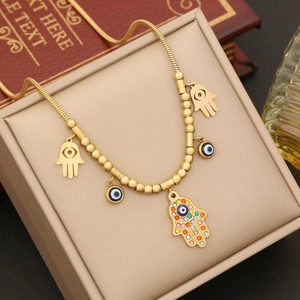 Golden snake chain necklace with Hamsa hand and evil eye charms in a jewelry box
