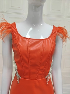 Détail d'une robe moulante orange vif avec épaules en plumes et glands en strass