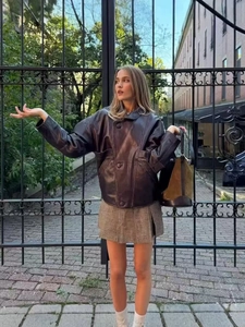 Street style view of oversized dark brown PU leather jacket paired with a plaid mini skirt
