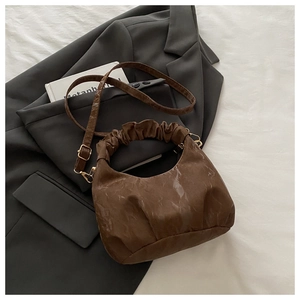 Detailansicht der braunen sichelförmigen Handtasche mit Falten und goldenen Beschlägen