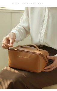 Brown leather cosmetic bag with top handle and gold lettering in soft studio lighting