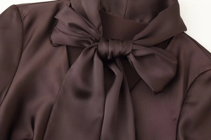 Detail of elegant dark brown satin dress featuring a large silk-textured bow at the neckline