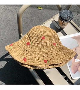 Detailed view of beige straw hat with small red strawberry embroidery in natural sunlight